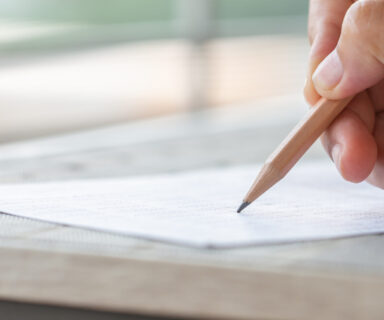 Student hand testing doing test exam with pencil drawing selected choices on answer sheet in school final exams at college or university. Taking multiple choice for assessment in examination classroom