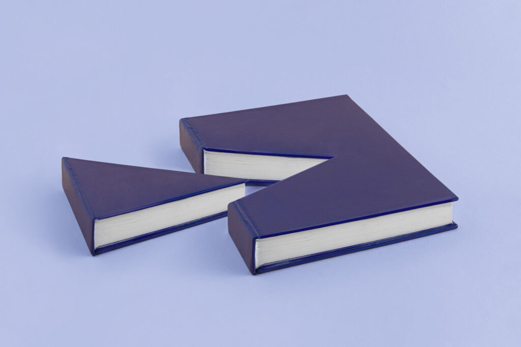 A-minimal-abstract-creative-scene-made-from-a-book-from-which-a-piece-was-cut.-Isolated-pastel-purple-blue-background-with-copy-space.-Cake-slice-concept.-Pleasure-of-reading.-Gift