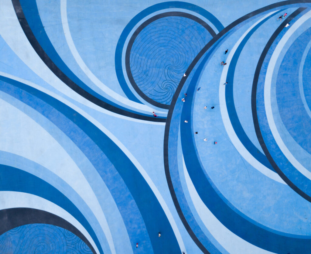 Aerial-Drone-View-of-People-walking-over-a-Circular-Swirl-Patterned-Blue-Floor