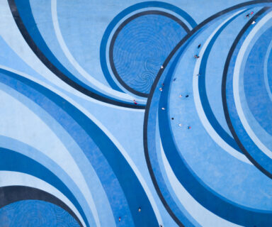 Aerial-Drone-View-of-People-walking-over-a-Circular-Swirl-Patterned-Blue-Floor