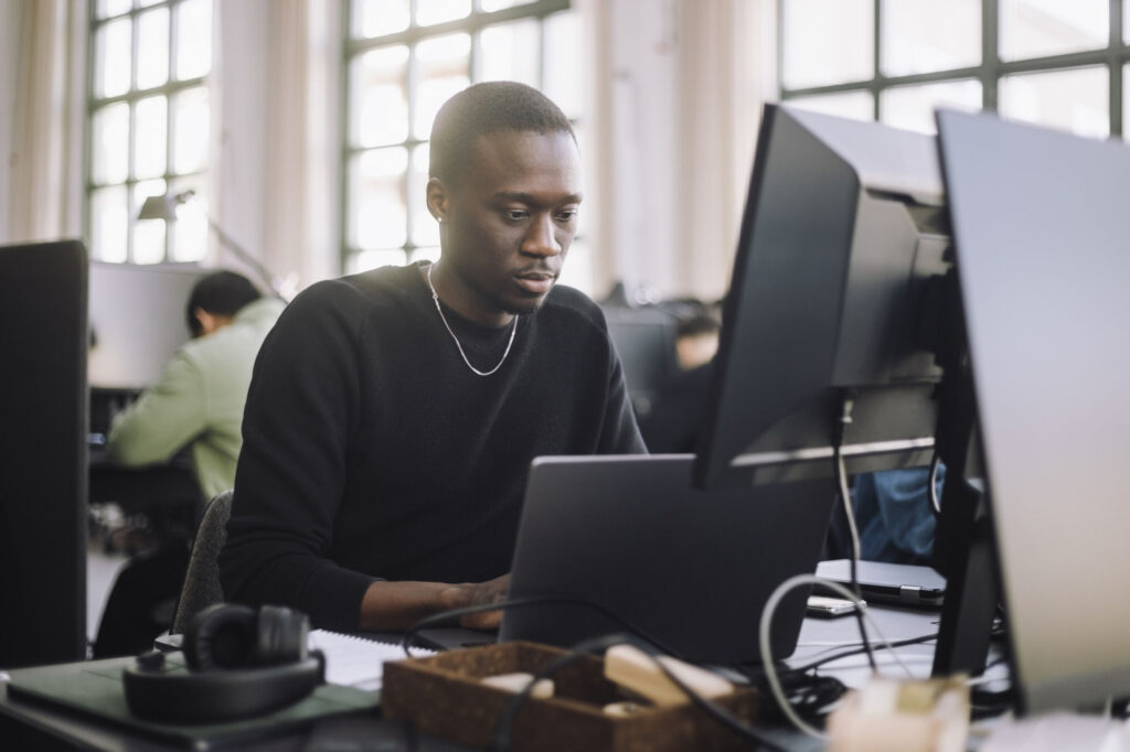 Focused-male-computer-programmer-working-on-laptop-at-desk-in-office