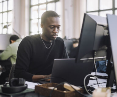 Focused-male-computer-programmer-working-on-laptop-at-desk-in-office