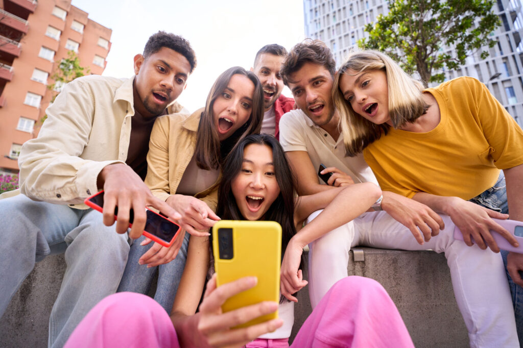 Group young people surprised watching something on phone. Multiracial friends outdoor using mobile.