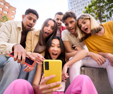 Group young people surprised watching something on phone. Multiracial friends outdoor using mobile.