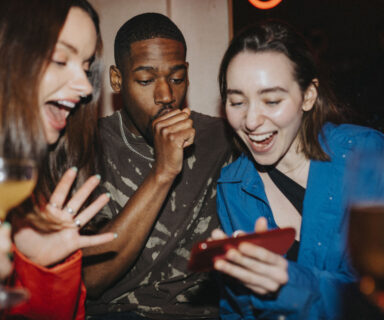 Happy woman sharing smart phone with male and female friends at nightclub