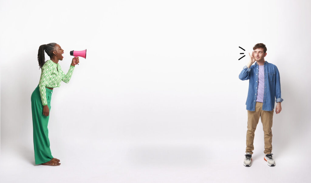 Mature-woman-talking-into-a-megaphone-while-young-man-holds-hand-to-ear-listening