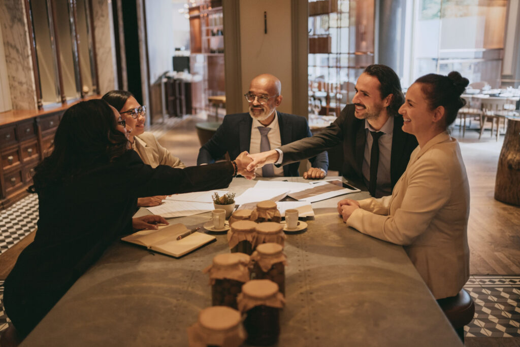 Smiling businessman and businesswoman handshaking colleagues at restaurant