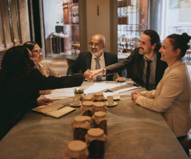 Smiling businessman and businesswoman handshaking colleagues at restaurant