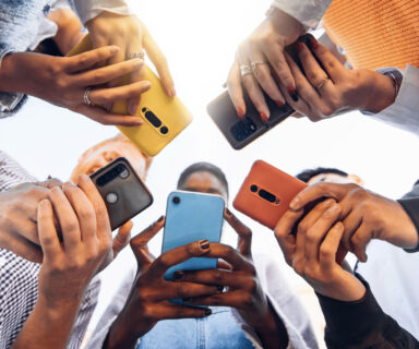 Teens-in-circle-holding-smart-mobile-phones-Multicultural-young-people-using-cellphones-outside-Teenagers-addicted-to-new-technology-concept