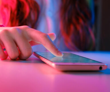 Use of mobile phone in trendy neon lights. Creative vivid color of ultraviolet red and blue. Hands of Teen Girl scrolling up photos Close-up at dark neon room. App for sale in shop. Social media. 4K