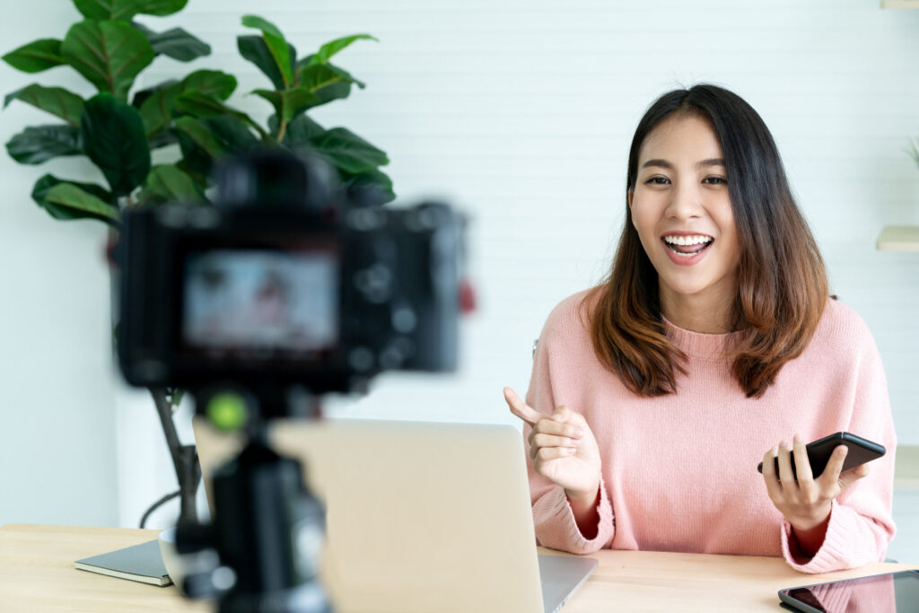 Young-attractive-asian-woman-blogger-or-vlogger-looking-at-camera-and-talking-on-video-shooting-with-technology.-Social-media-influencer-people-or-content-maker-concept-in-relax-ca