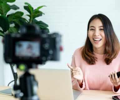 Young-attractive-asian-woman-blogger-or-vlogger-looking-at-camera-and-talking-on-video-shooting-with-technology.-Social-media-influencer-people-or-content-maker-concept-in-relax-ca